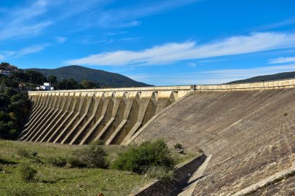 Vista ampla de uma grande barragem de concreto sob céu azul, representando infraestrutura hídrica.