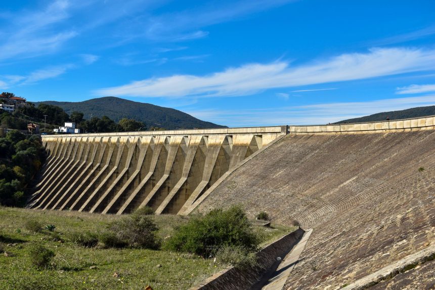 Vista ampla de uma grande barragem de concreto sob céu azul, representando infraestrutura hídrica.