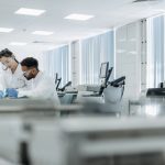 Dois pesquisadores trabalham em um laboratório de alta tecnologia, usando óculos e luvas de proteção.