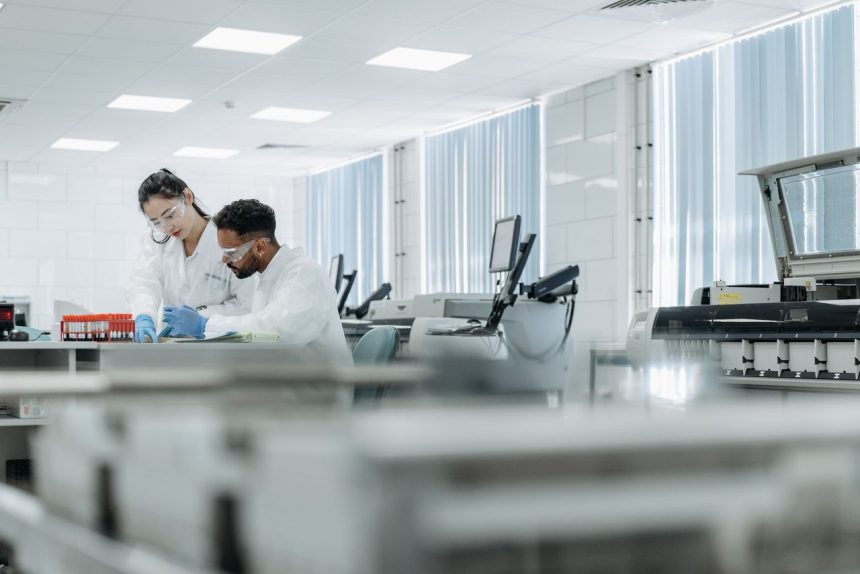 Dois pesquisadores trabalham em um laboratório de alta tecnologia, usando óculos e luvas de proteção.